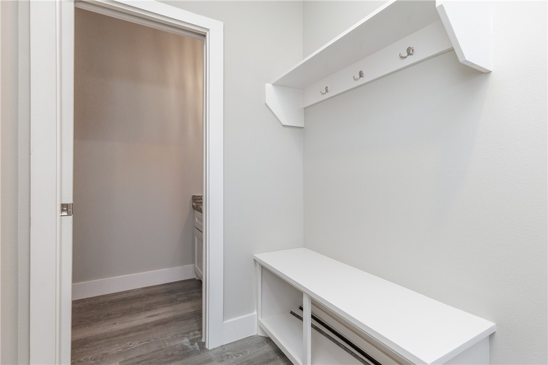 White entry nook with a built-in bench and three hooks above, beside an open doorway.