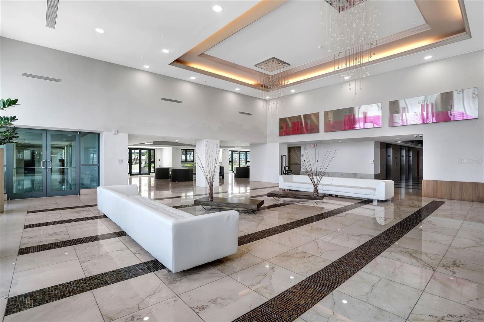 Modern condominium lobby with glossy patterned marble floors, white sofas, and a cascading chandelier.
