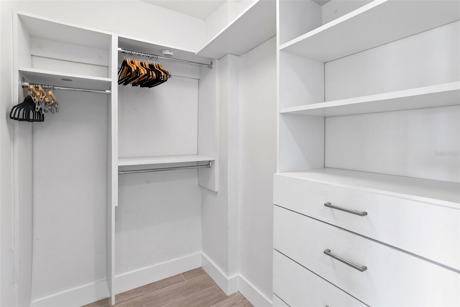 Walk-in closet with white built-in shelves and drawers and empty hangers.