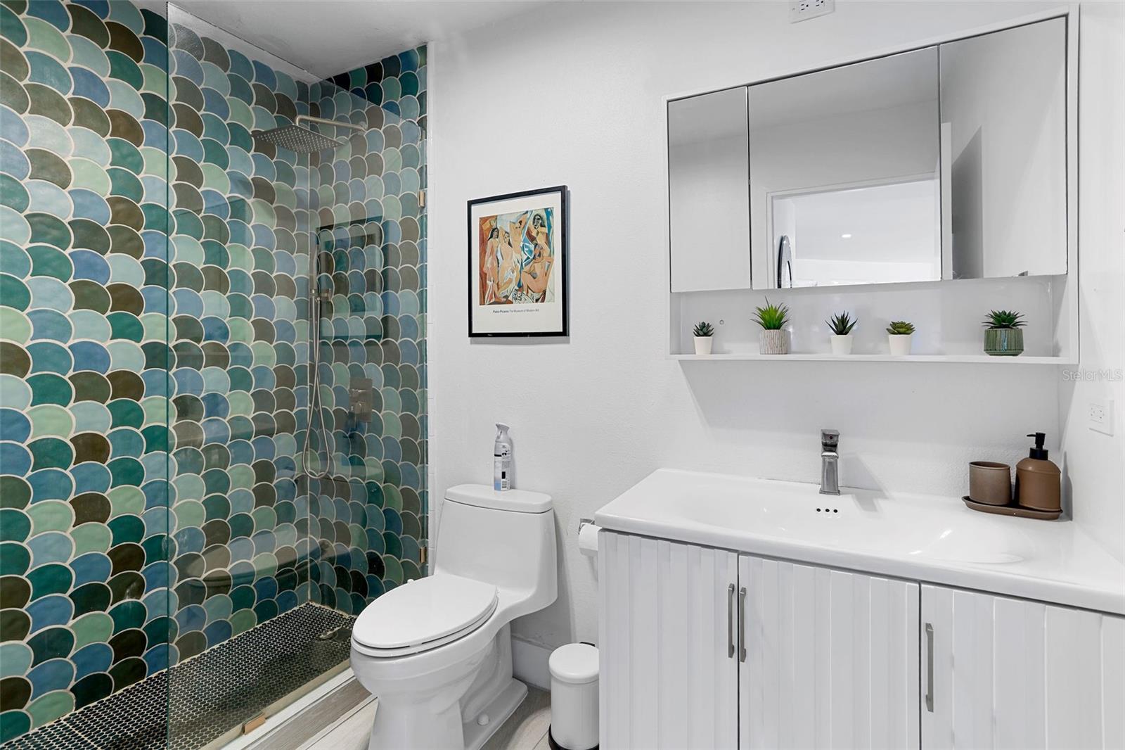 Bathroom with a teal scallop-tile shower, white toilet, and vanity with mirrored cabinet.