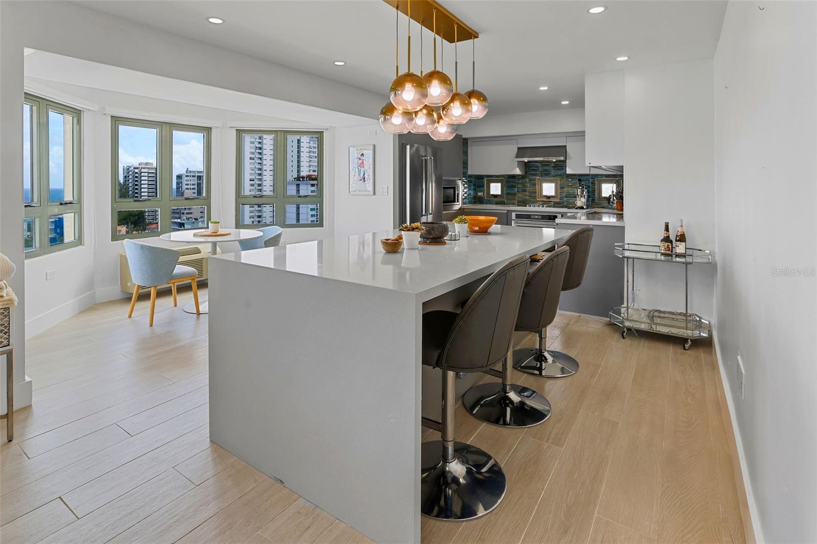 Open kitchen with a large island, pendant lights, and windows overlooking buildings and the ocean.