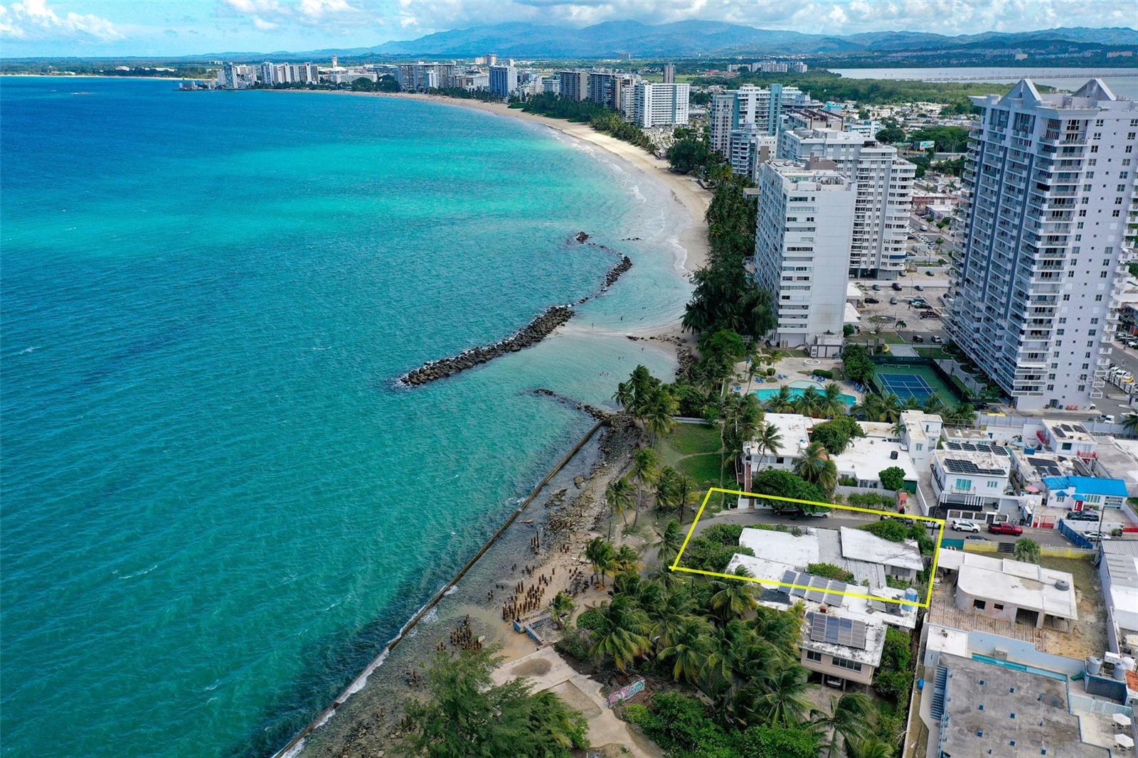 Coastal lot outlined in yellow beside turquoise water, a rocky beach, and beachfront apartment towers.
