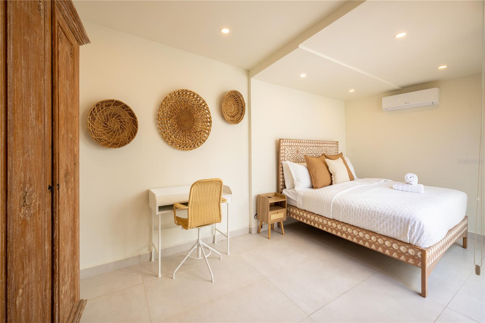 Bedroom with a patterned wooden bed, woven wall decor, and a small desk and chair.