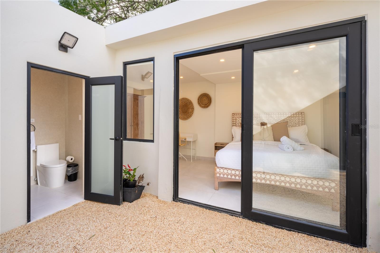 Patio outside a furnished bedroom, with black-framed sliding doors and an open bathroom doorway.