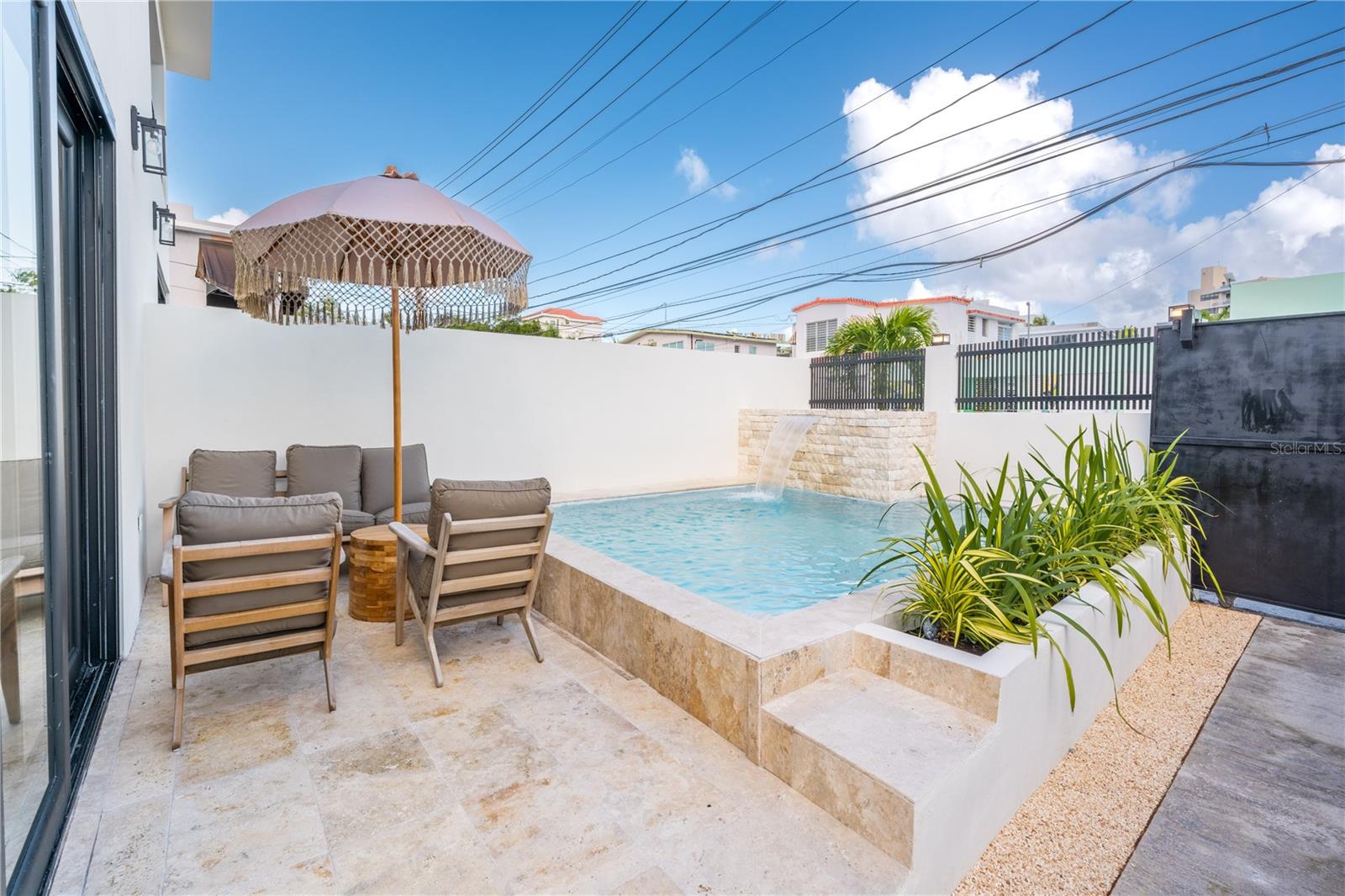 Private patio pool with a stone waterfall and cushioned lounge chairs beneath a fringed umbrella.