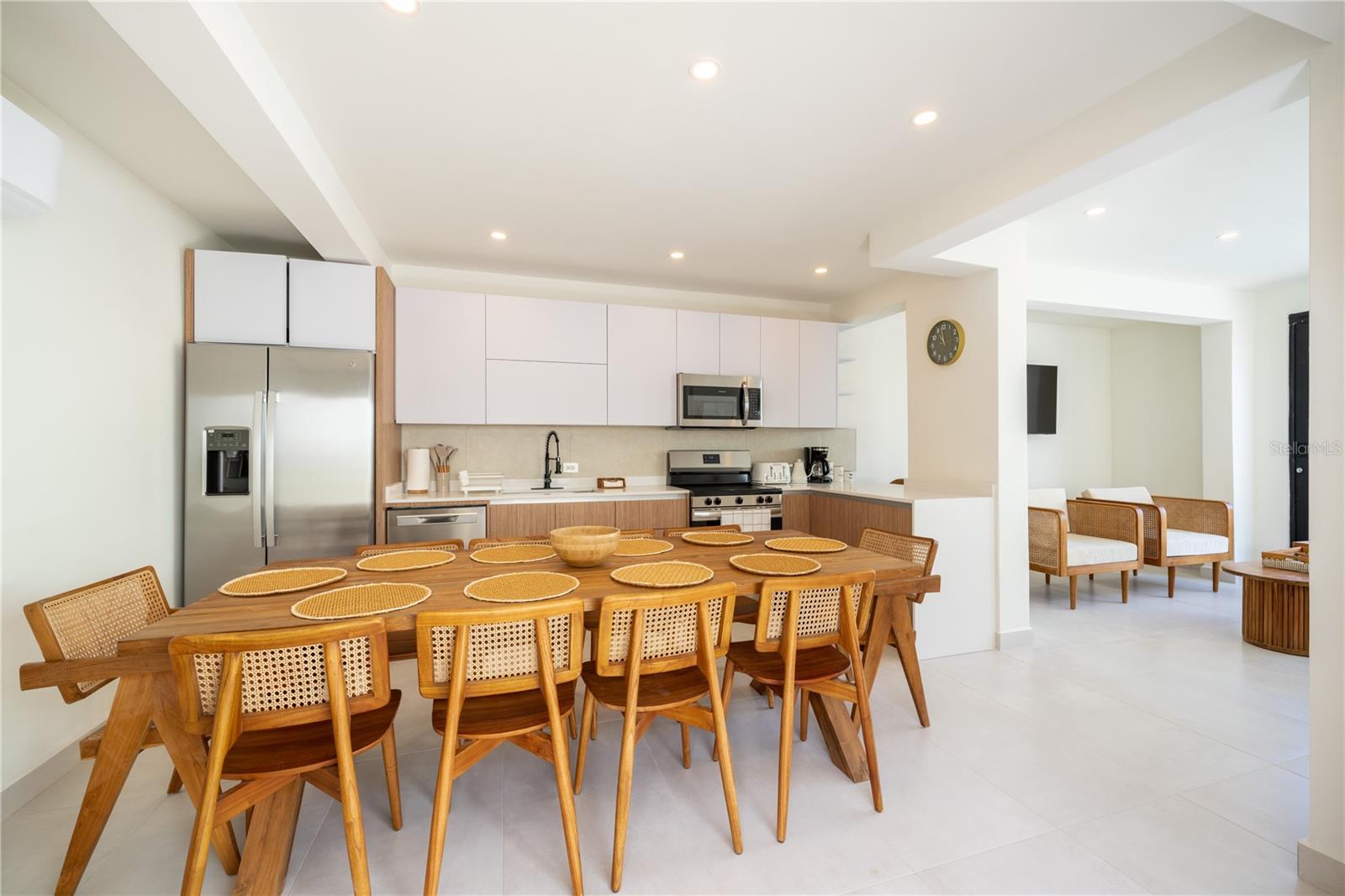 Open-plan kitchen and dining area with white cabinetry, stainless steel appliances, and a long wooden table.