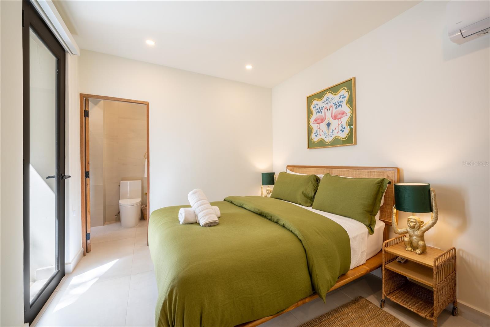 Bedroom with an olive-green king bed, wicker headboard, and open doorway to a bathroom.
