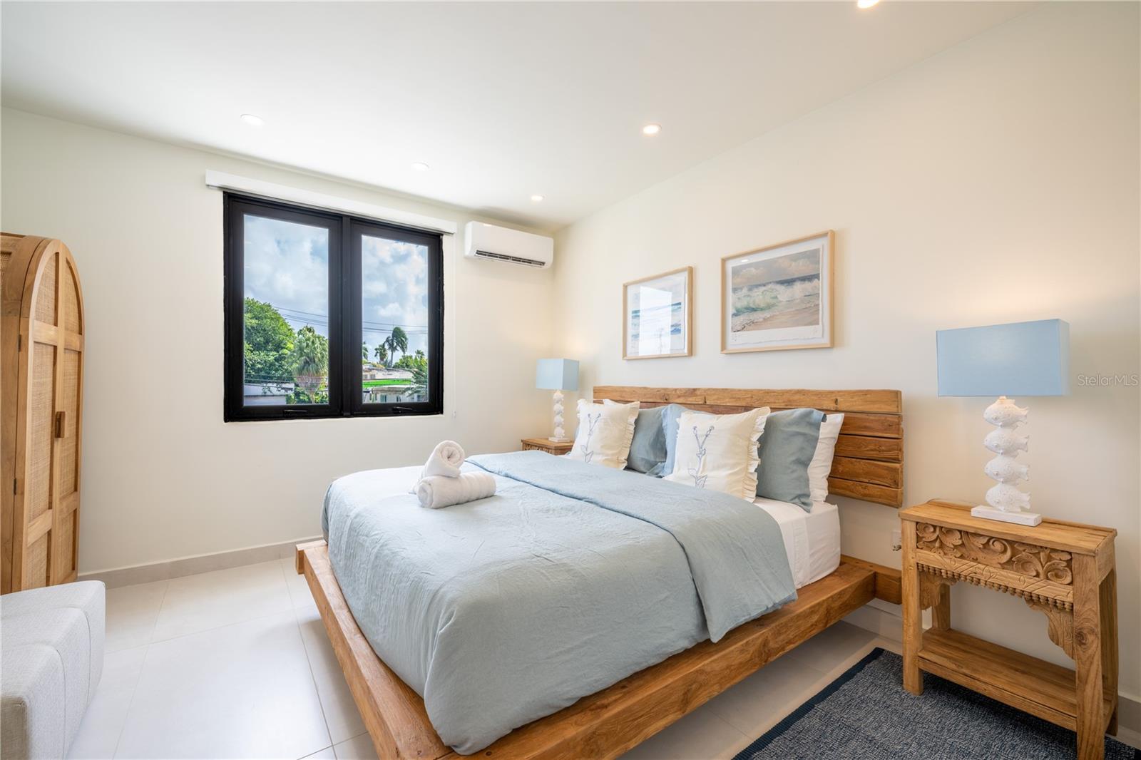 Bedroom with a wooden platform bed, pale blue bedding, carved nightstands, and a window overlooking trees.