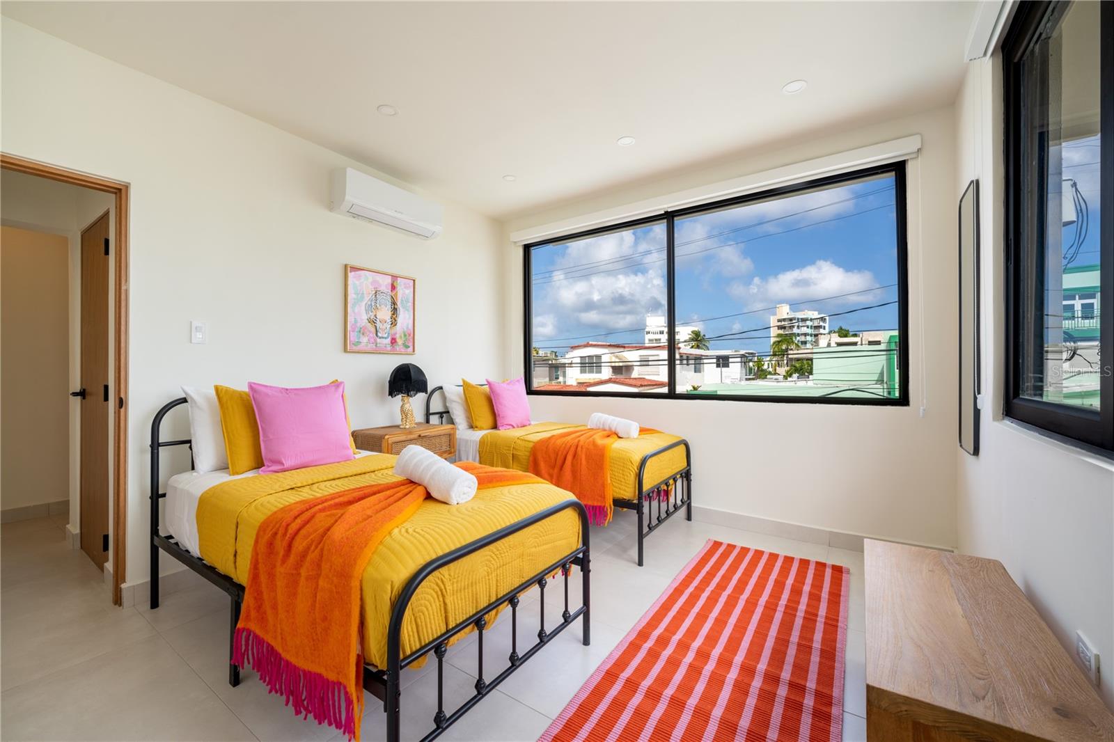 Bedroom with two twin beds in bright yellow bedding and large windows overlooking nearby buildings.