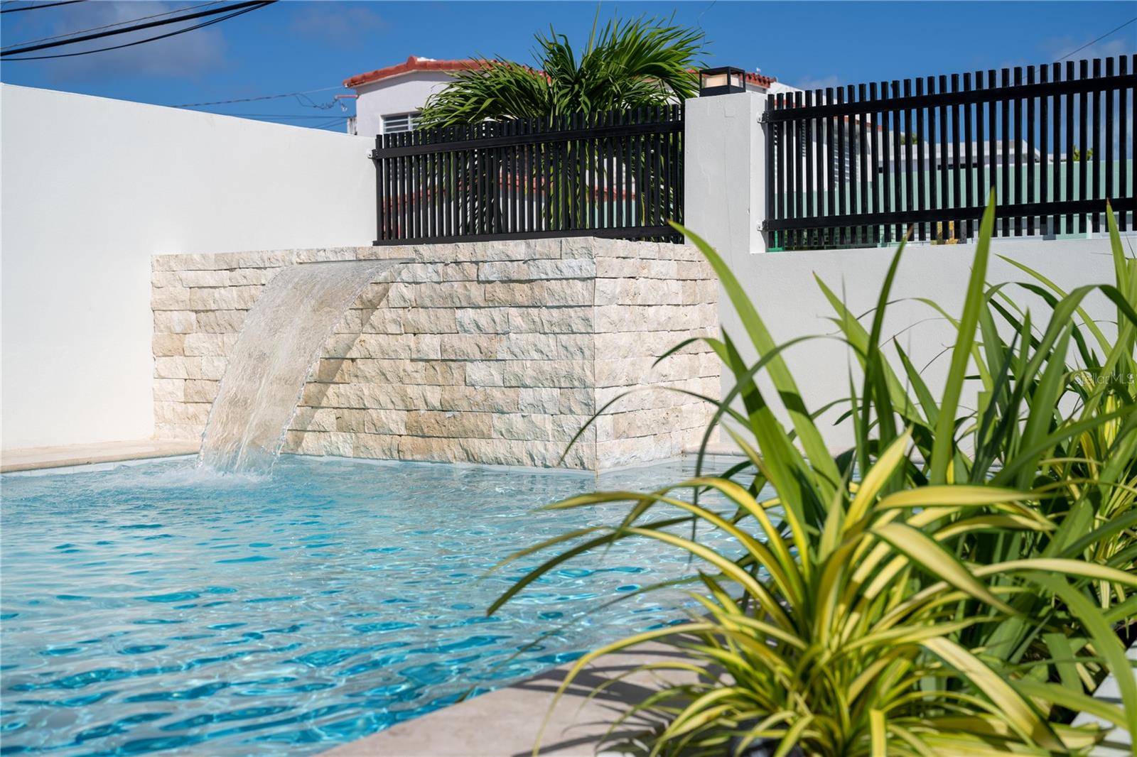 Outdoor pool with a stone waterfall feature and tropical plants in the foreground.
