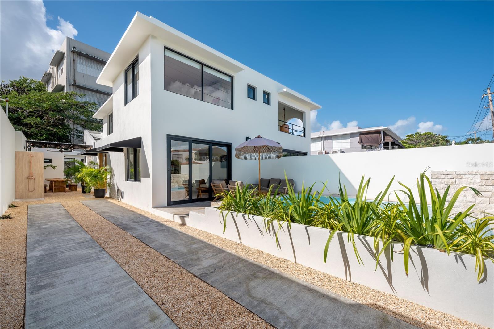 Modern white two-story house with a walled patio, tropical landscaping, and outdoor seating.