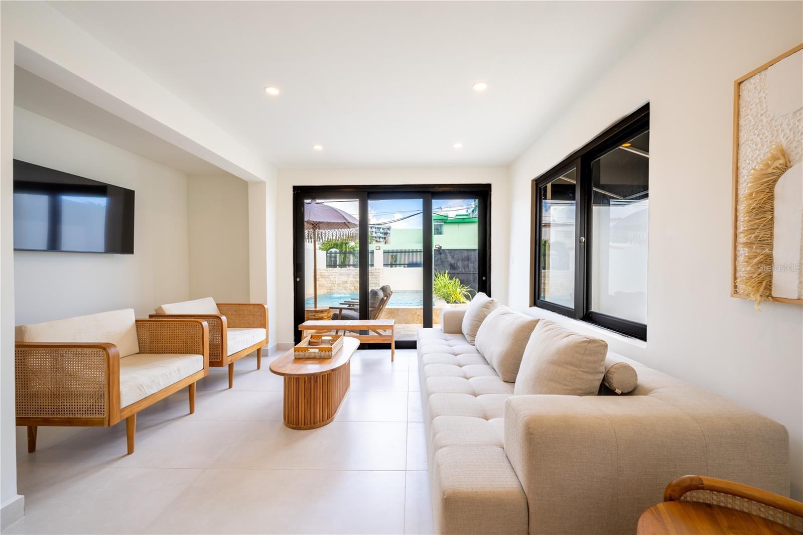 Living room with a beige sectional and cane chairs facing glass doors to a pool.