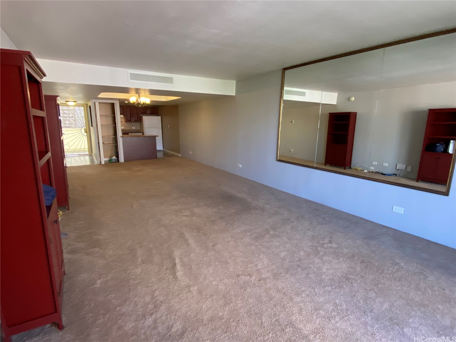 Living room with beige carpet, red built-in shelving, a large mirror, and an open kitchen.