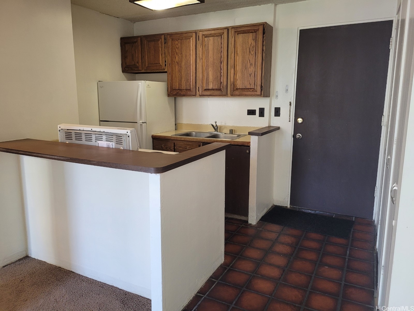 Compact kitchen with wood cabinets, a refrigerator, sink, and tiled entry floor.