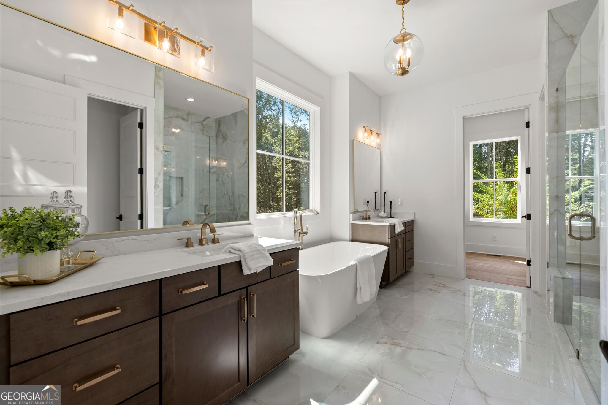 Bright bathroom with a dark double vanity, freestanding tub, and glass-enclosed shower.