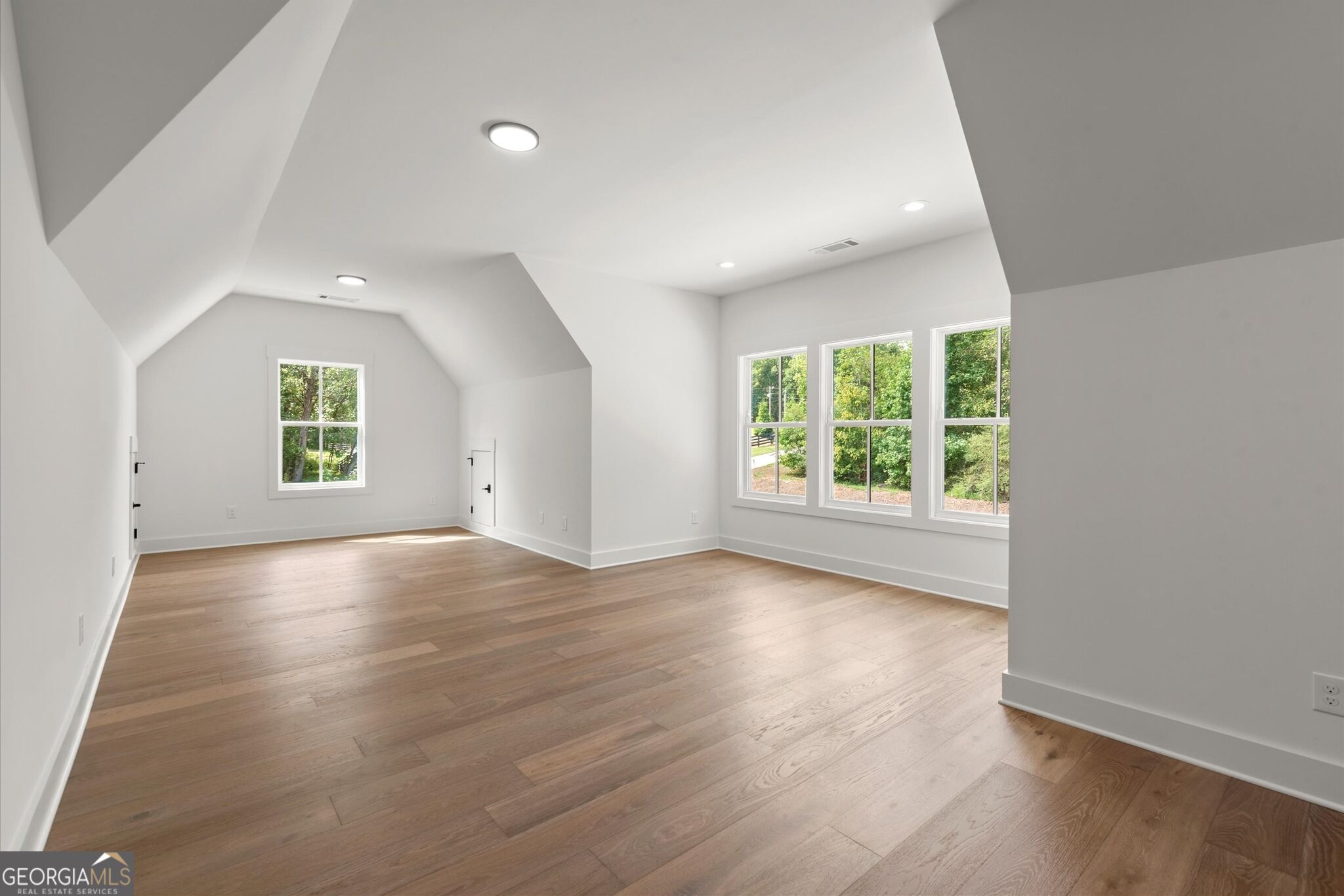 Empty room with hardwood floors, a high angled ceiling, and four windows.