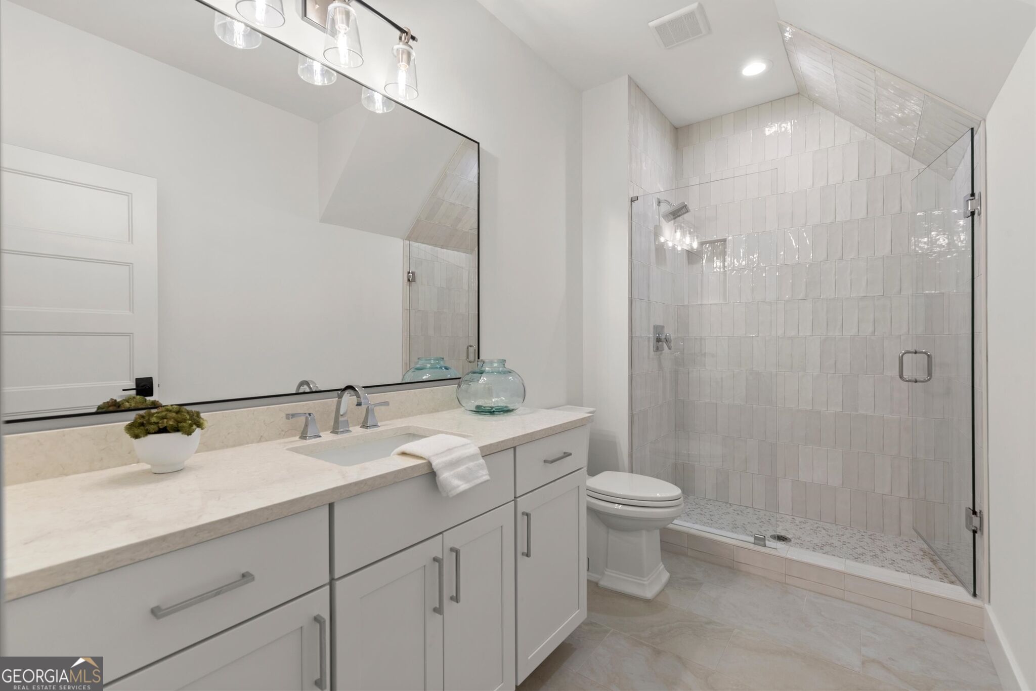 Bathroom with a long white vanity and glass-enclosed tiled walk-in shower.