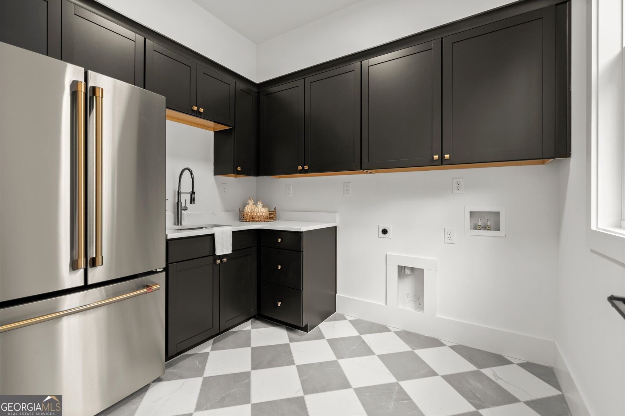 Laundry room with black cabinets, stainless steel appliances, white sink, and gray-and-white checkered floor.