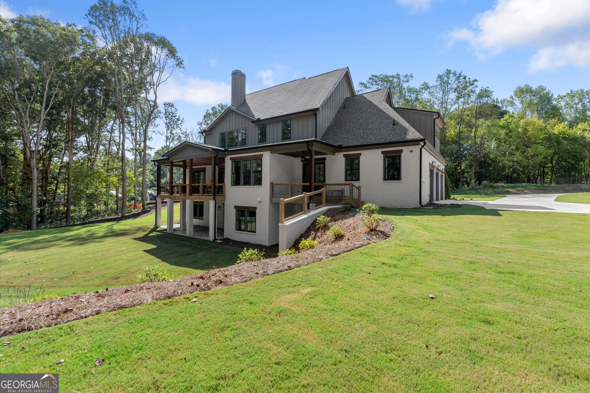 Two-story house with a covered wooden deck, attached garage, and broad sloping lawn.