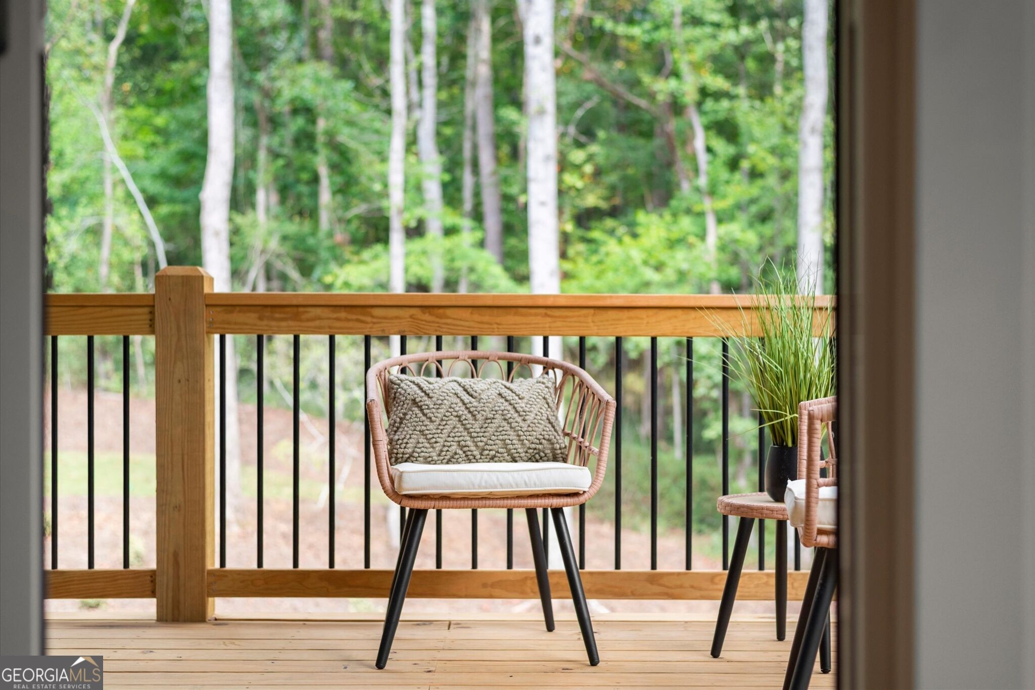 Wooden deck with wicker chairs overlooking a leafy wooded area.