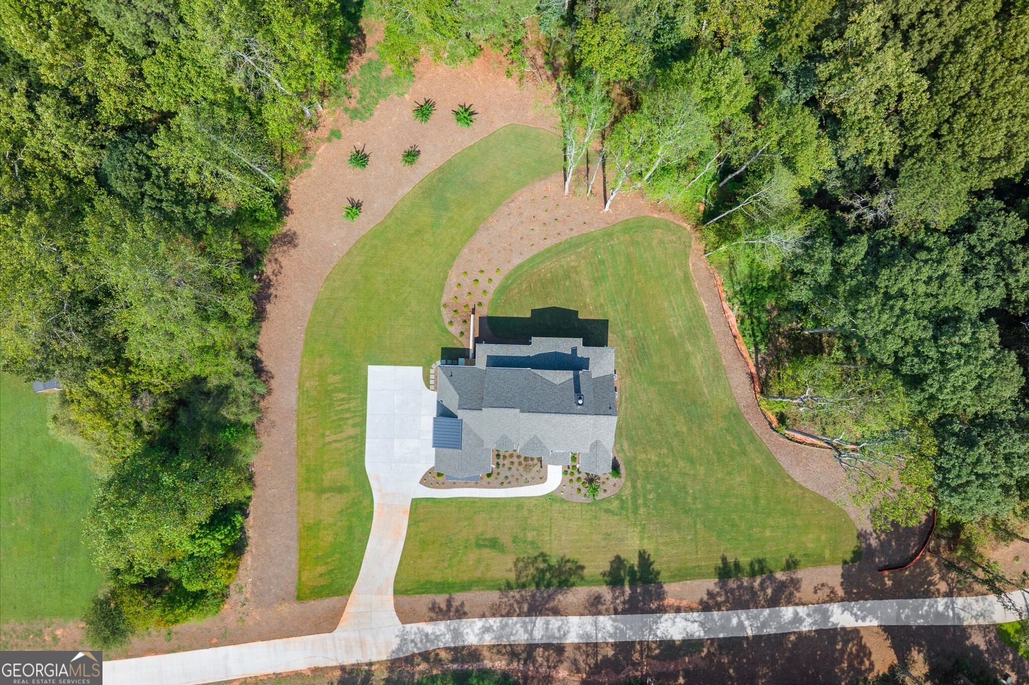 Aerial view of a house with a broad lawn, mature trees, and a curving driveway.