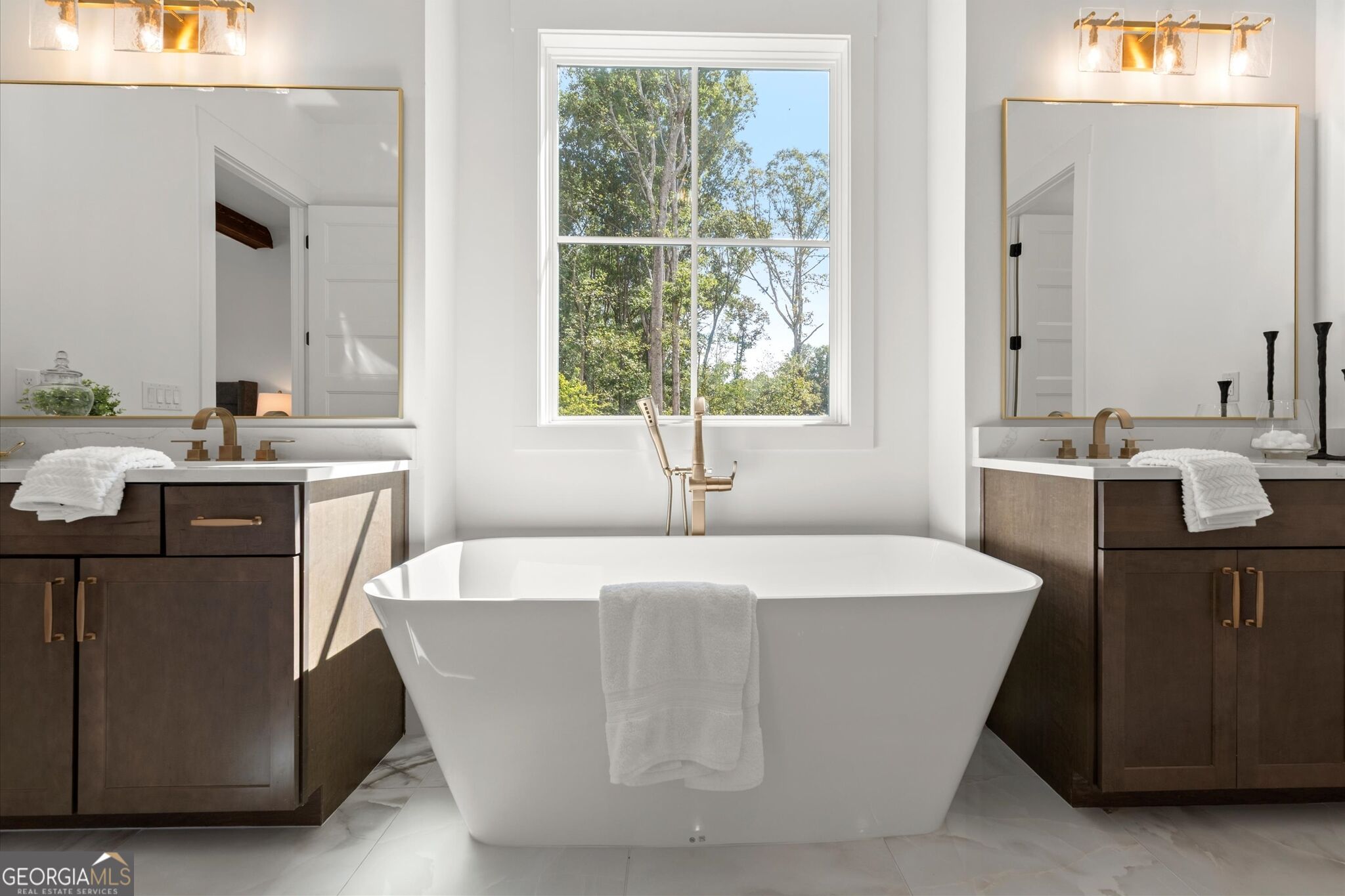 Primary bathroom with a freestanding tub beneath a large window and matching dark wood vanities.