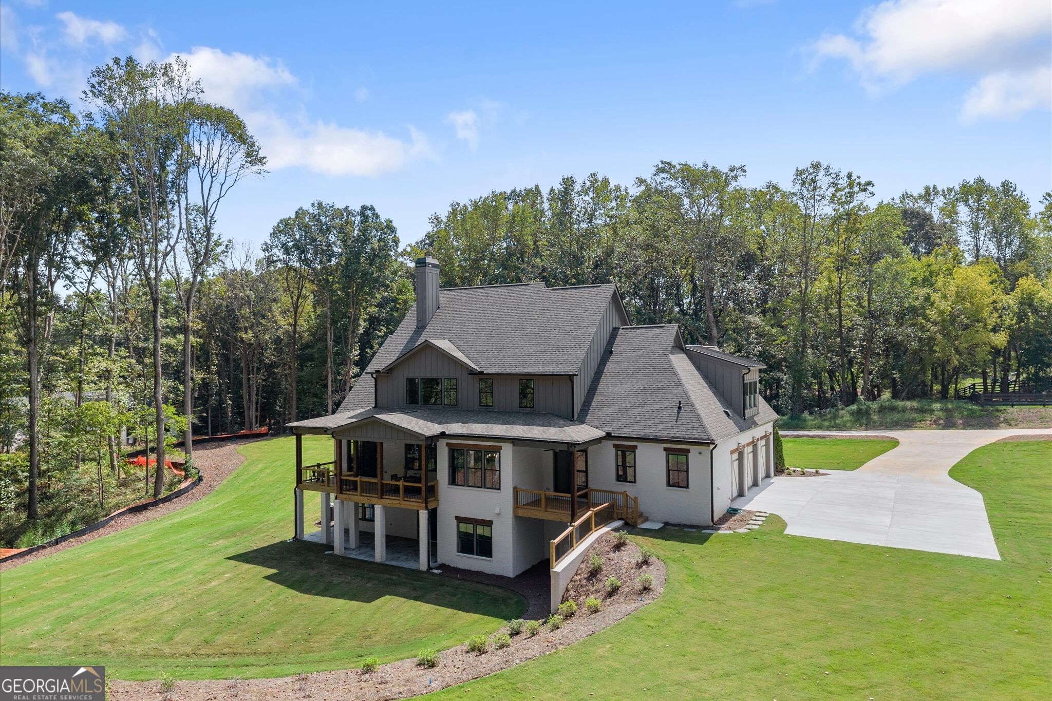 Rear exterior of a gray multi-level house with covered wooden porches, a broad lawn, and a curved driveway.