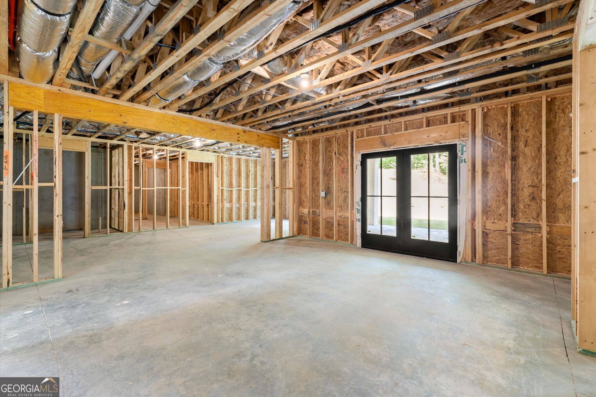 Unfinished interior with exposed framing, concrete floor, and black-framed glass double doors.
