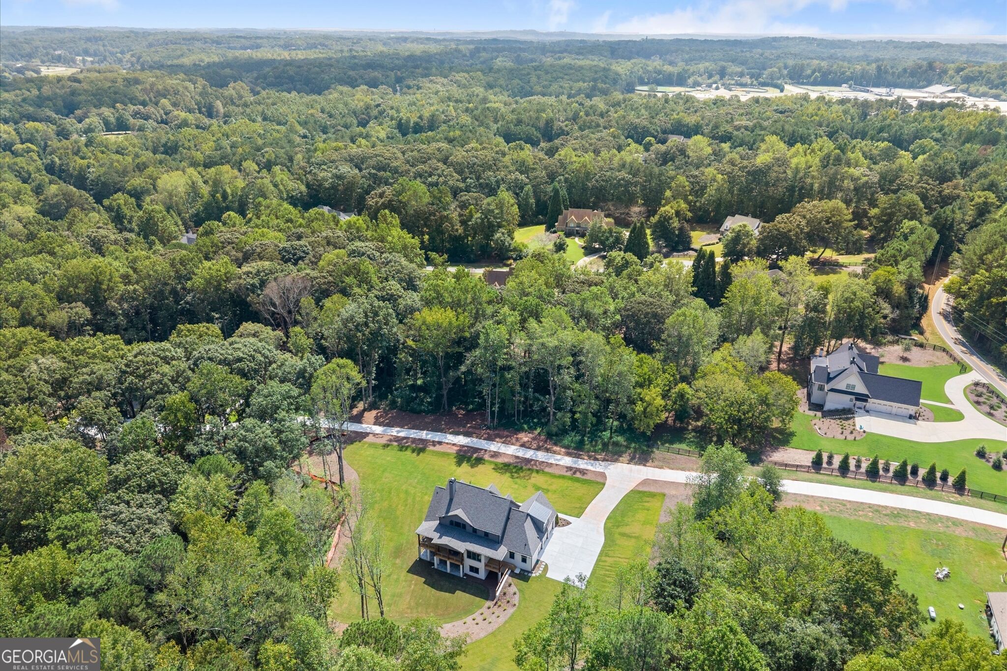Aerial view of a house on a landscaped lot surrounded by dense woodland and neighboring homes.
