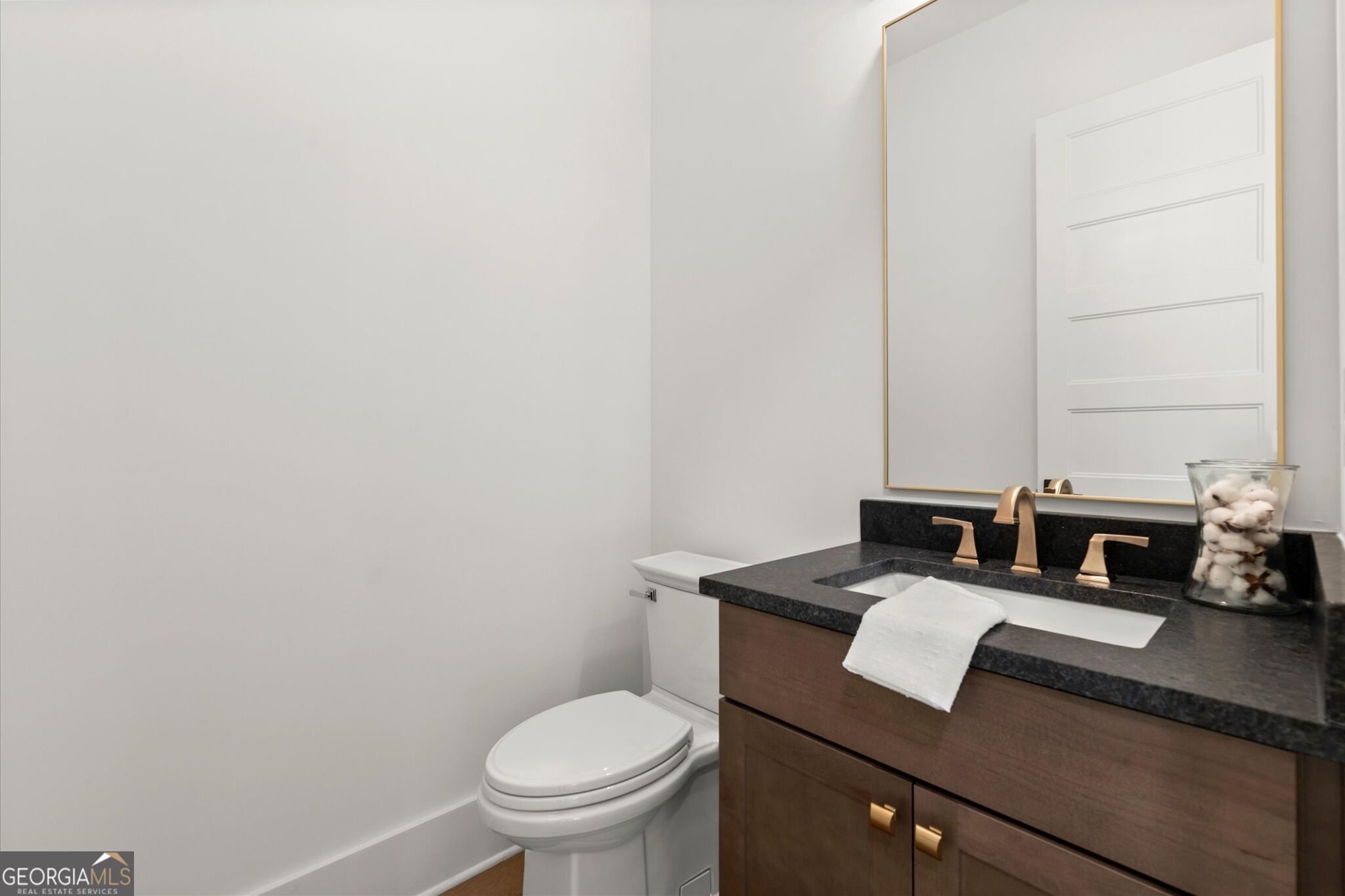 Bathroom with a dark stone vanity, bronze faucet, wood cabinetry, and white toilet.