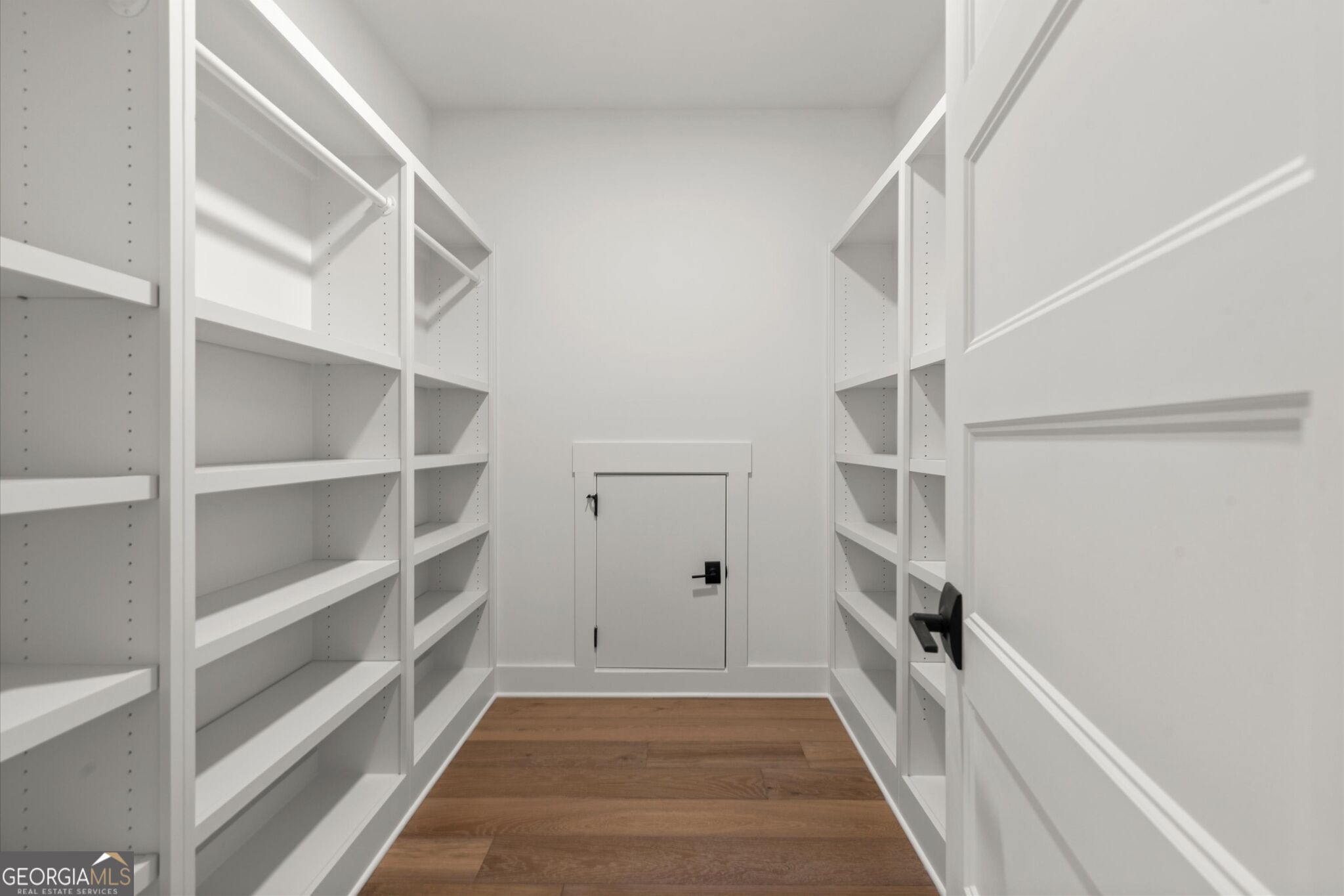 Walk-in closet with white built-in shelving, hanging rods, and wood flooring.