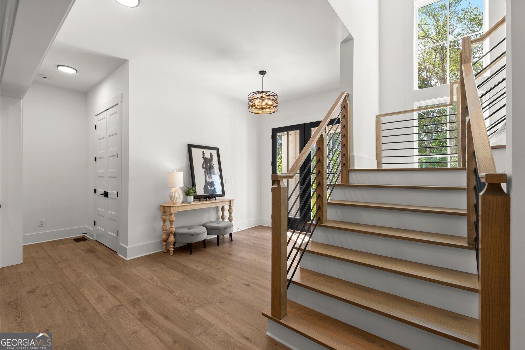 Entry foyer with a wood staircase, black metal railings, and tall windows.