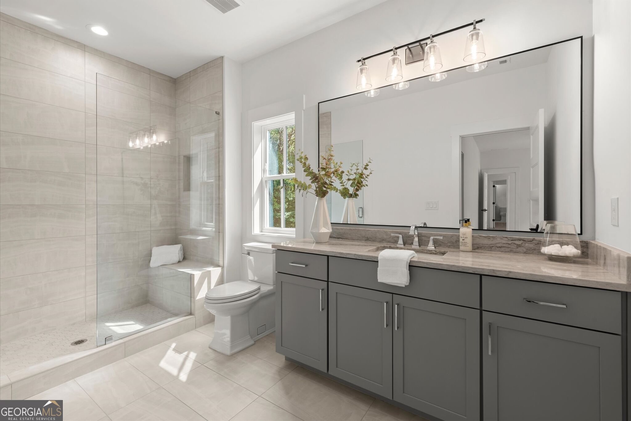 Modern bathroom with a glass walk-in shower, gray vanity, and large mirror.