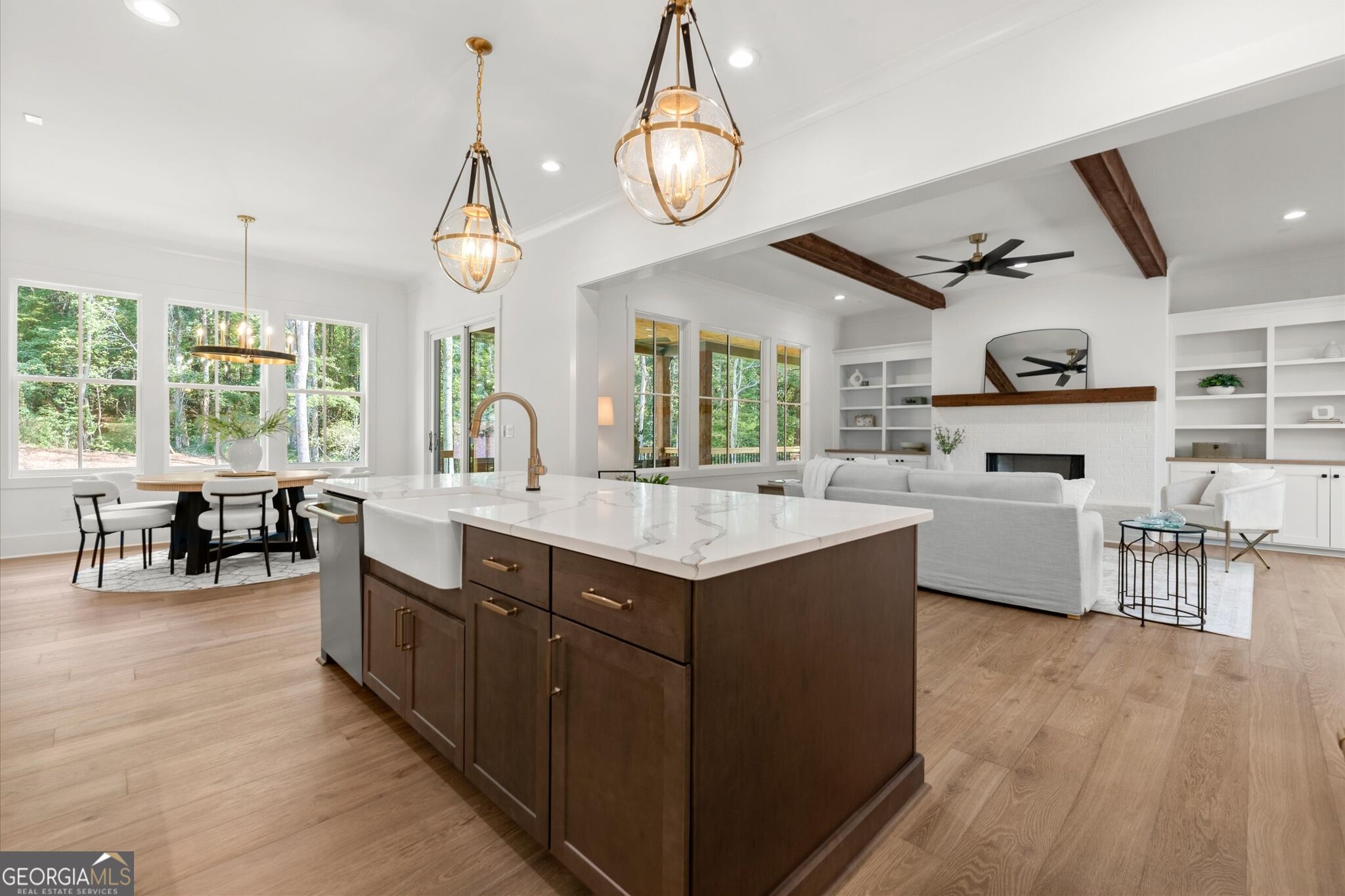 Open-plan kitchen and living room with a dark wood island, brass pendants, and exposed ceiling beams.