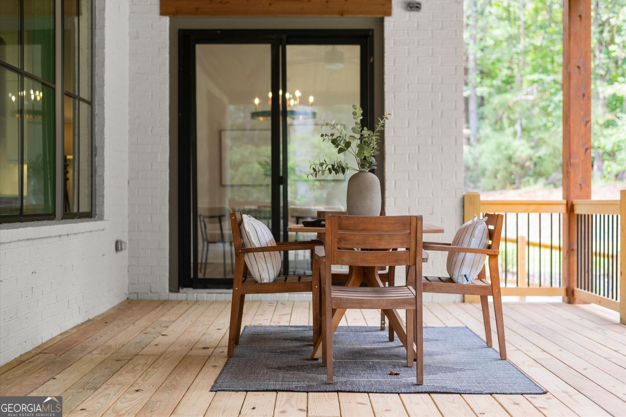 Covered deck with a wooden dining set, gray rug, white brick walls, and leafy views.