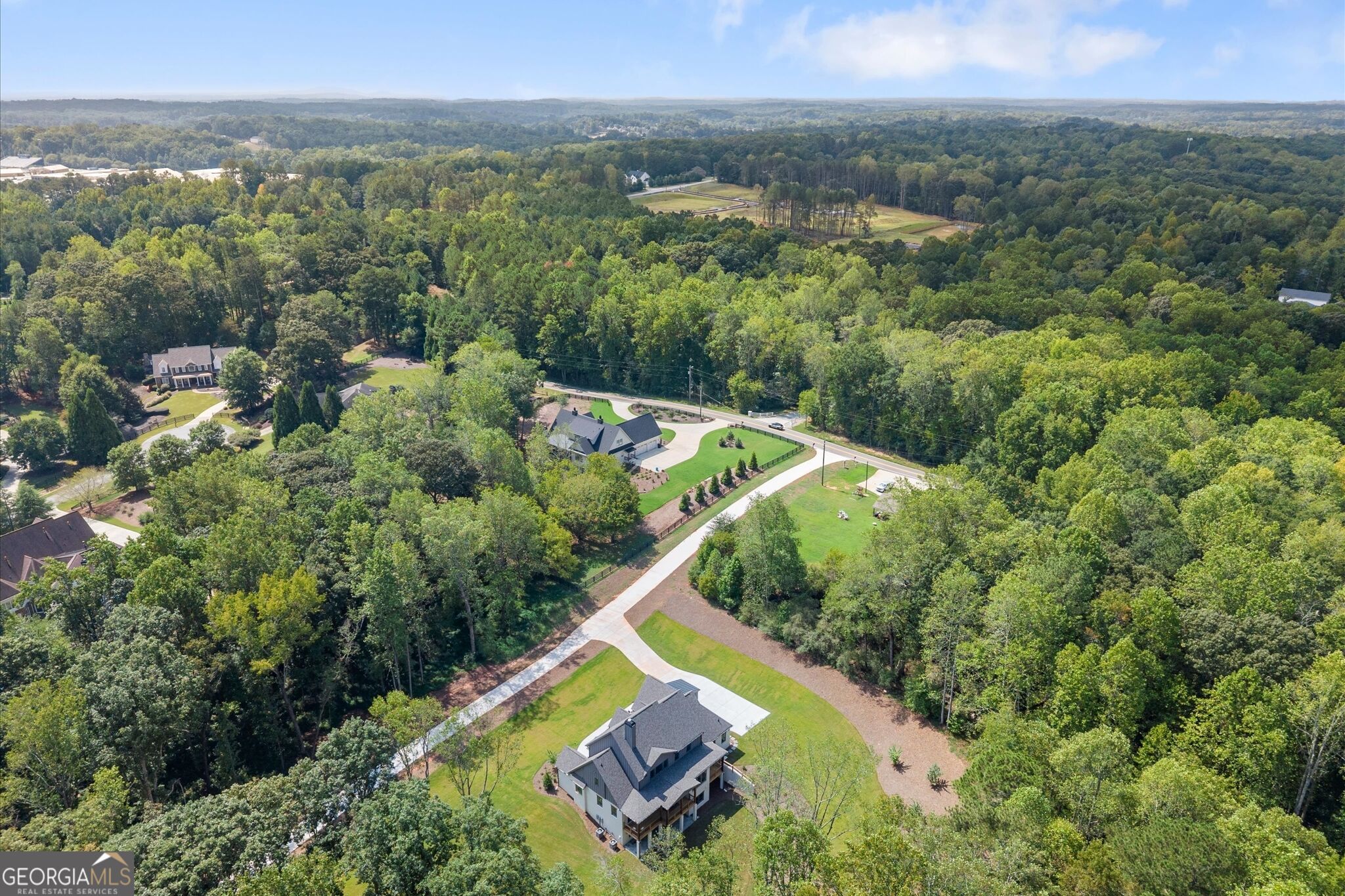 Aerial view of a house surrounded by trees, with a long driveway leading to the road.