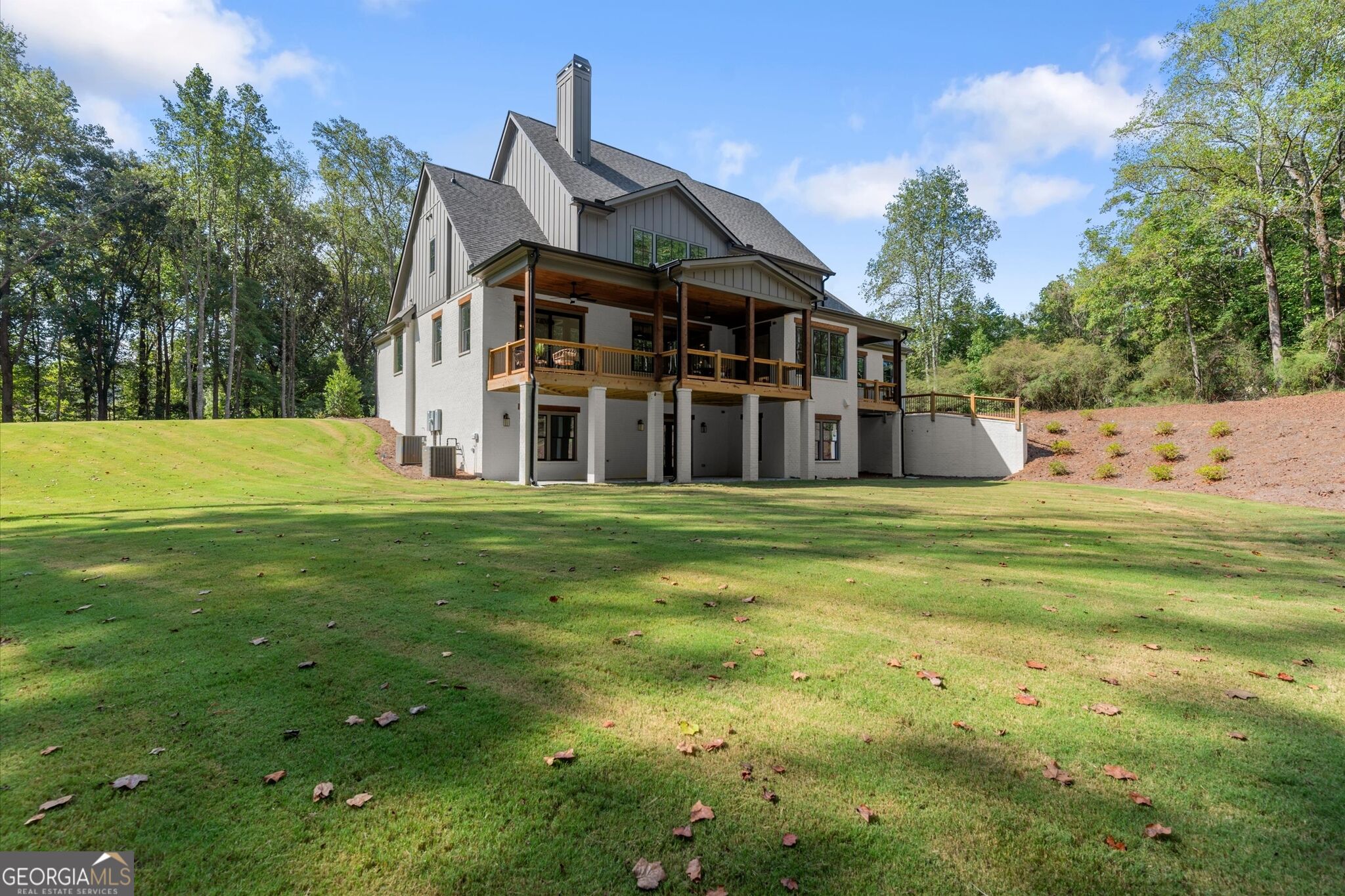 Rear of a multi-level home with a covered deck overlooking a broad lawn and wooded surroundings.