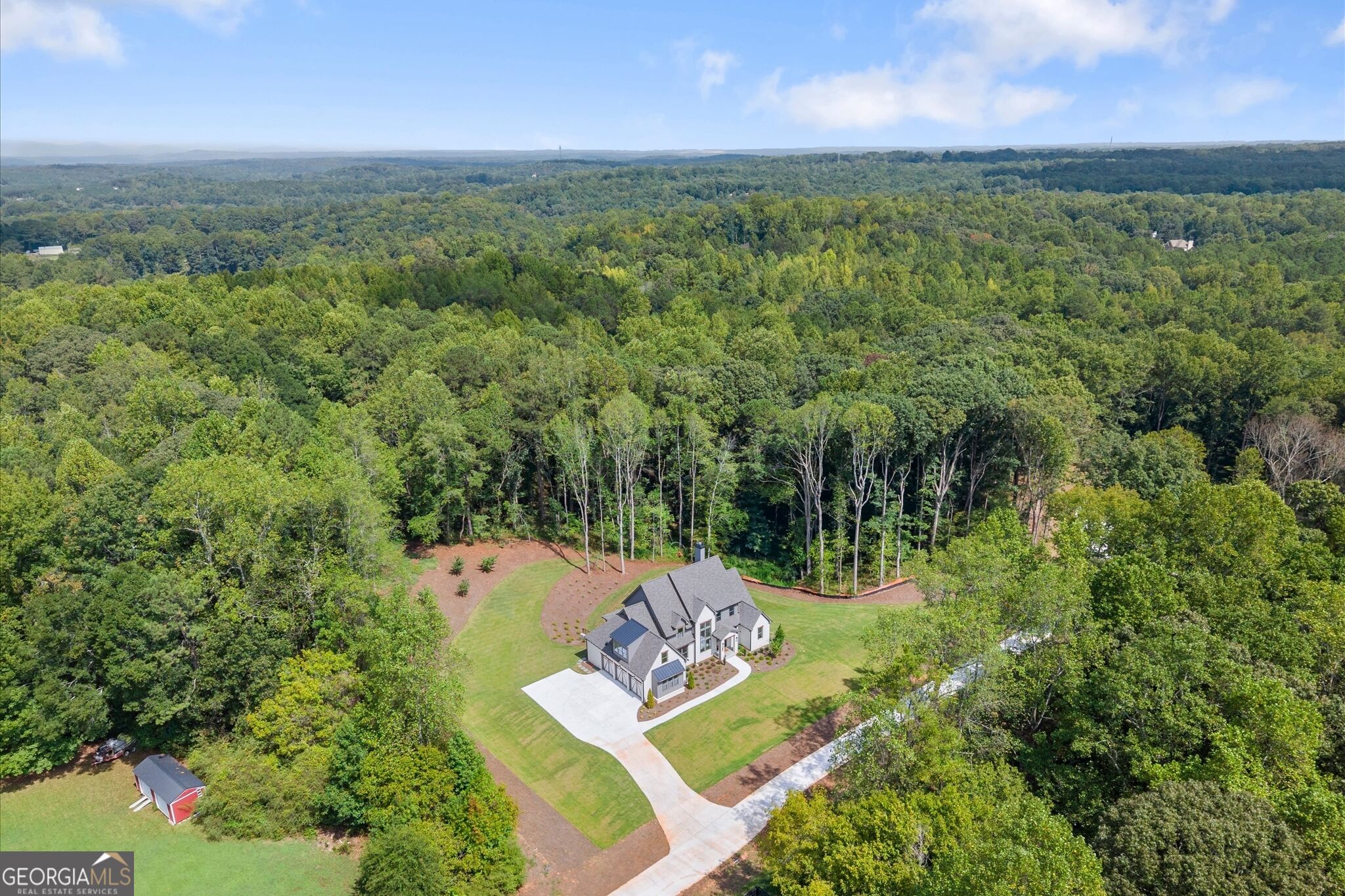 Aerial view of a house with a curved driveway, broad lawn, and surrounding woodland.