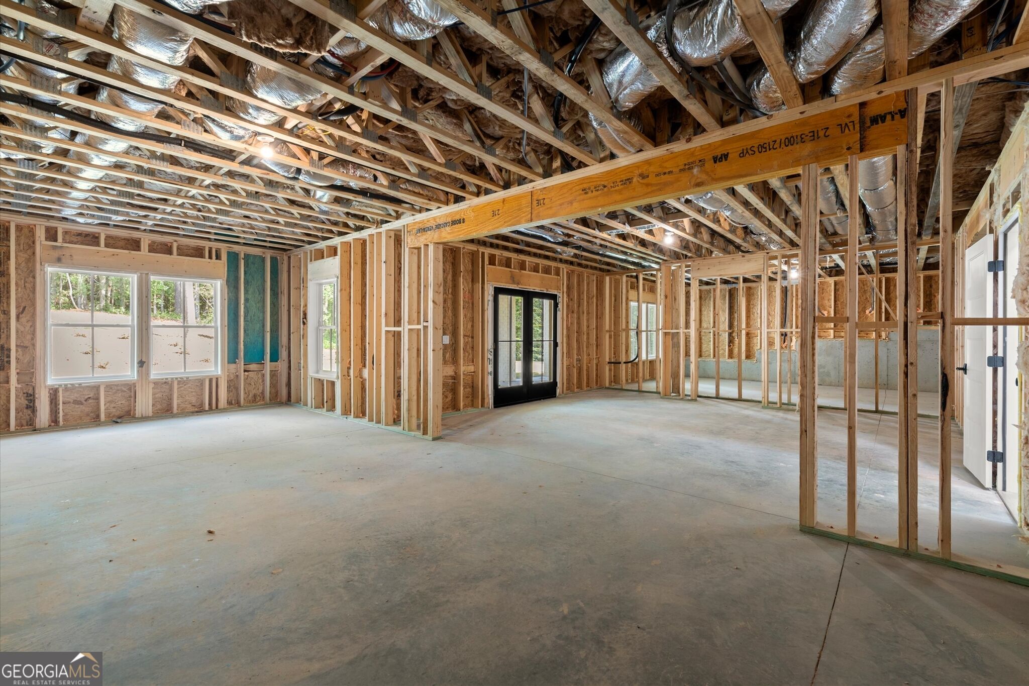 Unfinished home interior with exposed framing, overhead ductwork, and black-framed glass doors.