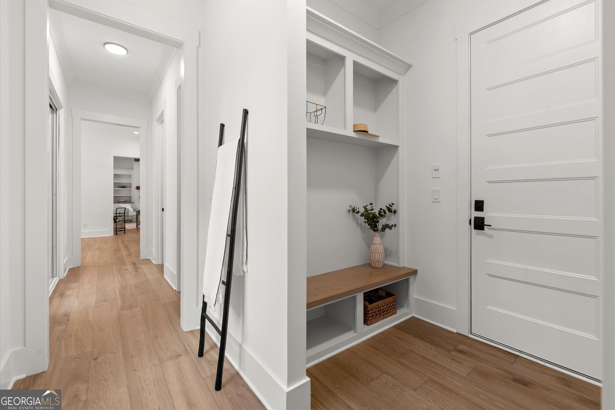 Entryway with a built-in bench and cubbies beside the front door, opening onto a wood-floored hallway.