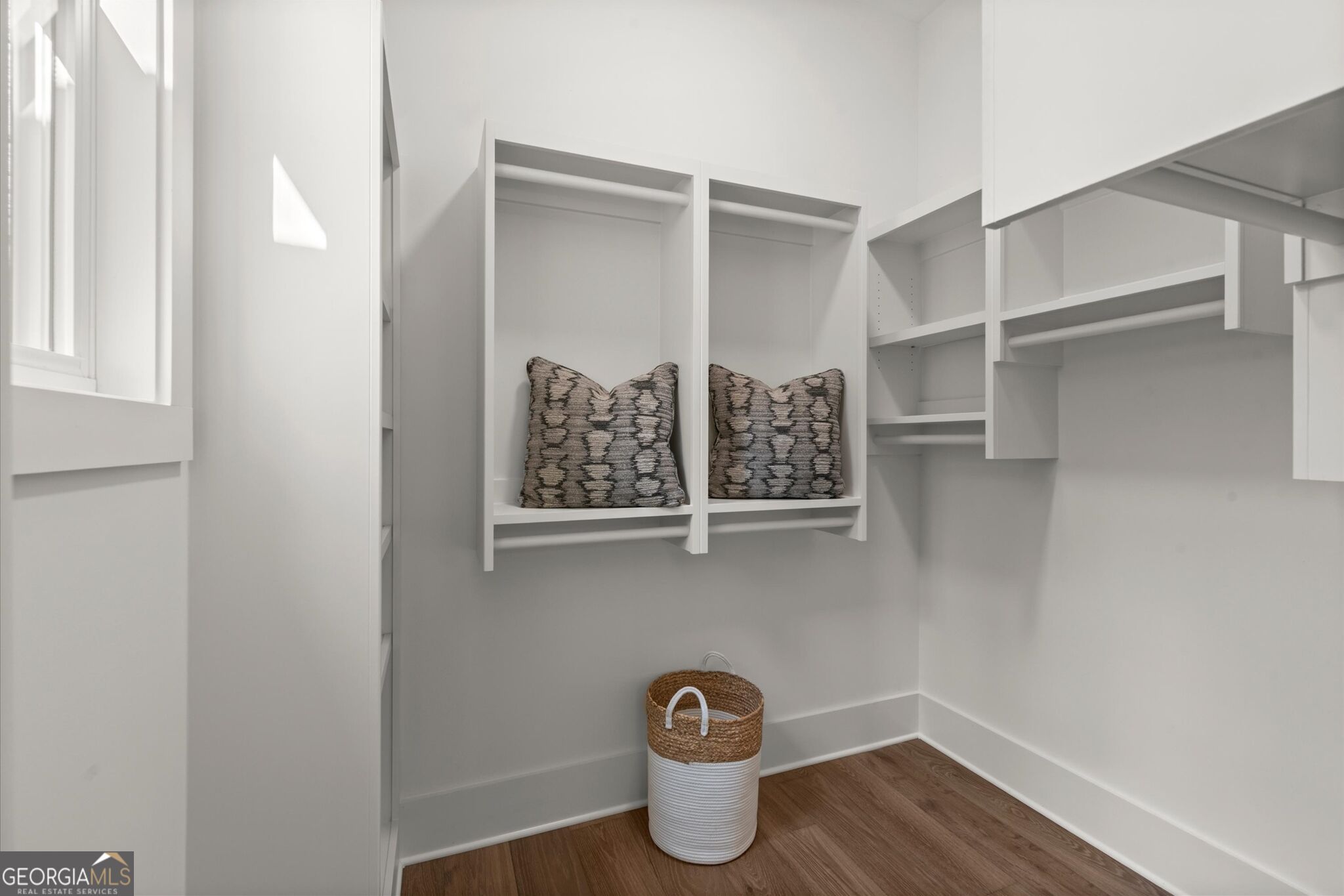 Walk-in closet with white built-in shelving, patterned pillows, and a woven laundry basket.