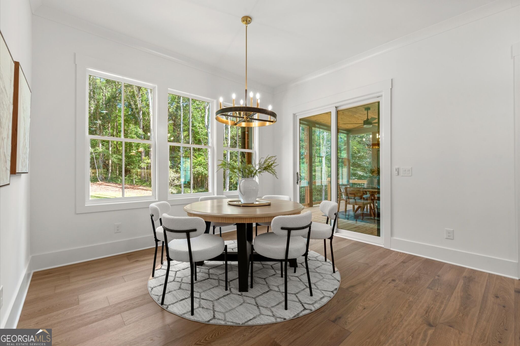 Dining room with a round table and chandelier beside large windows overlooking trees.