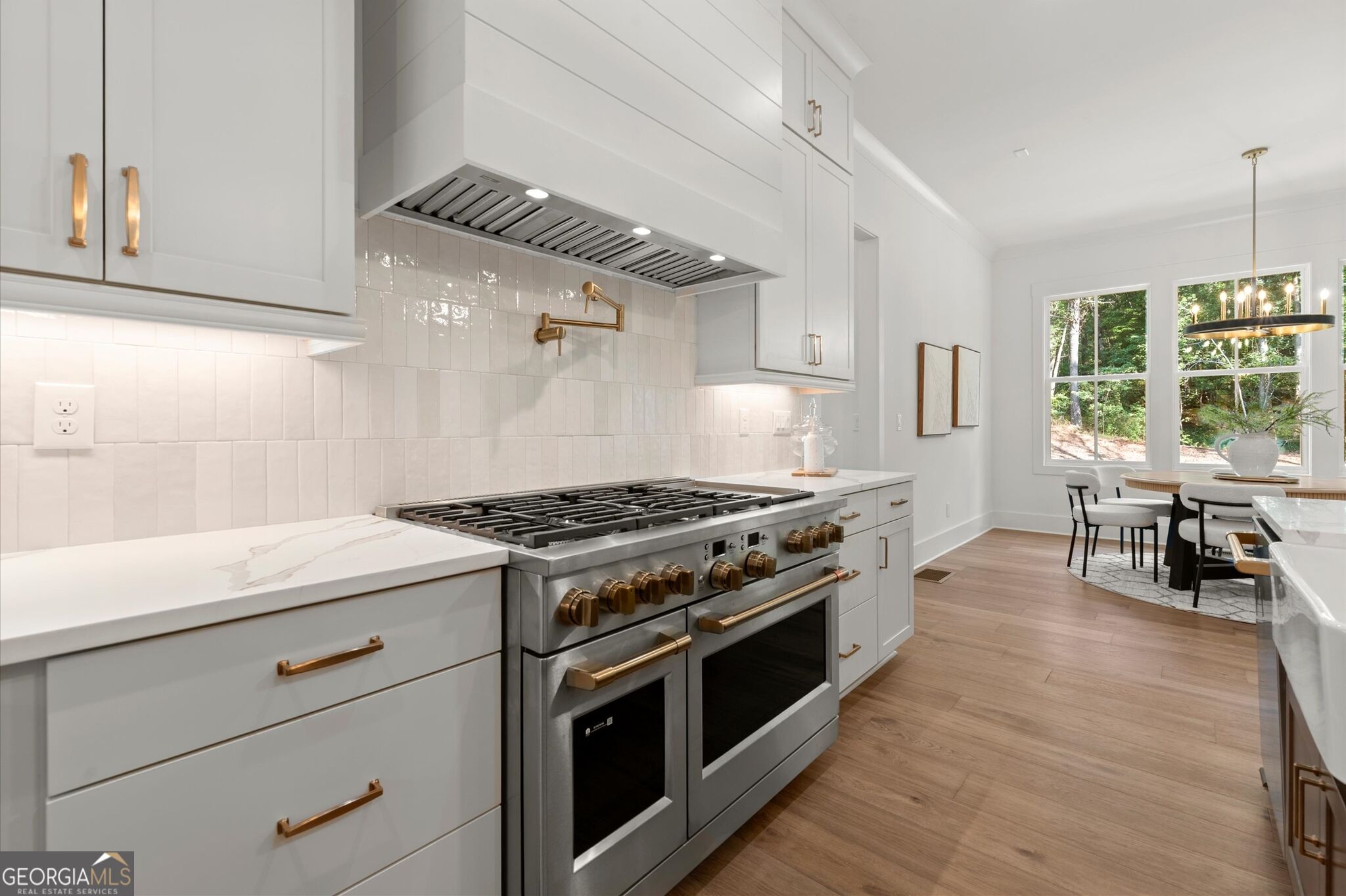 Bright white kitchen with a stainless steel range, brass hardware, and an adjoining dining area.