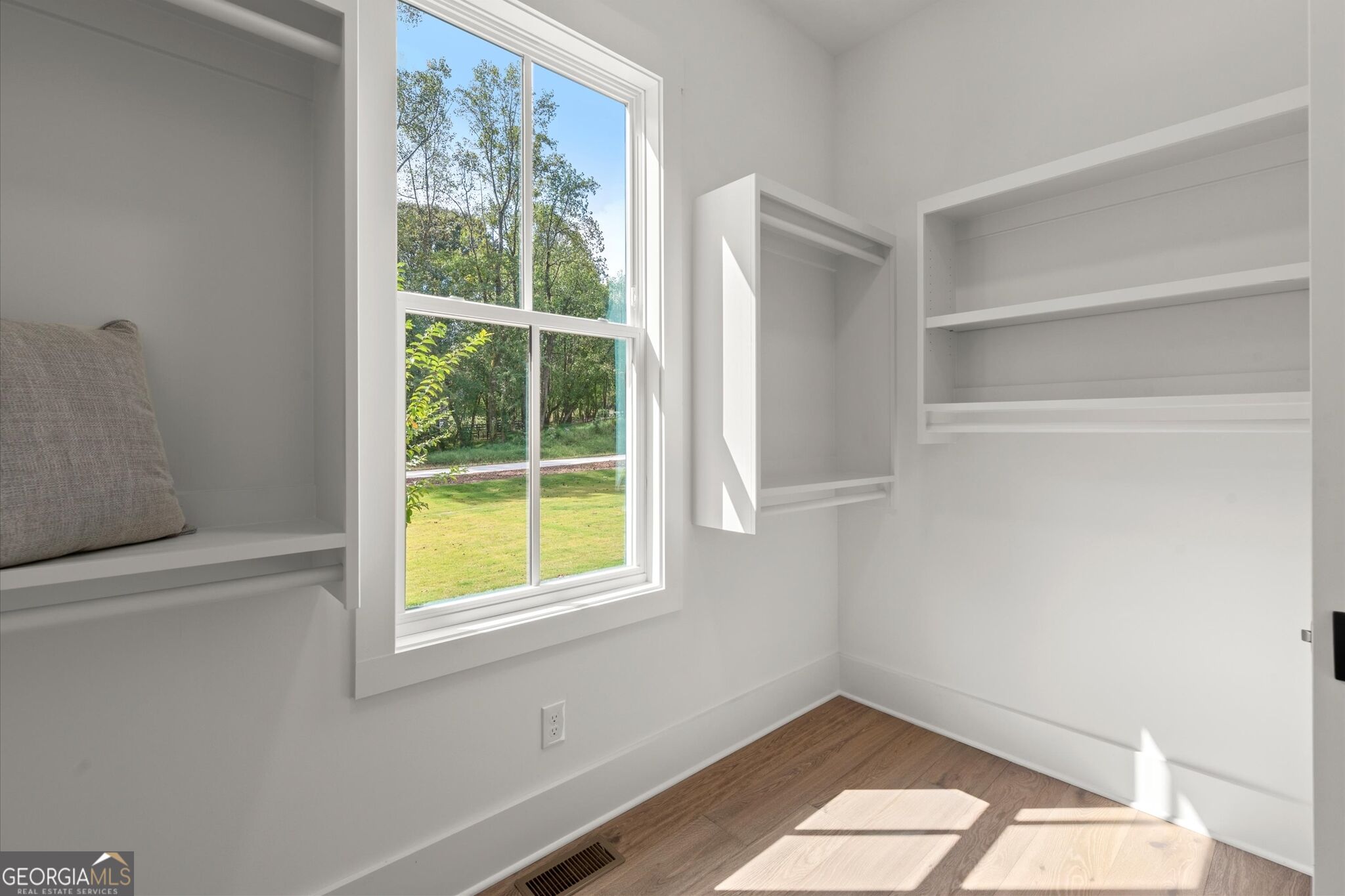 Bright room with built-in shelves, a window overlooking trees, and sunlight on the wood floor.