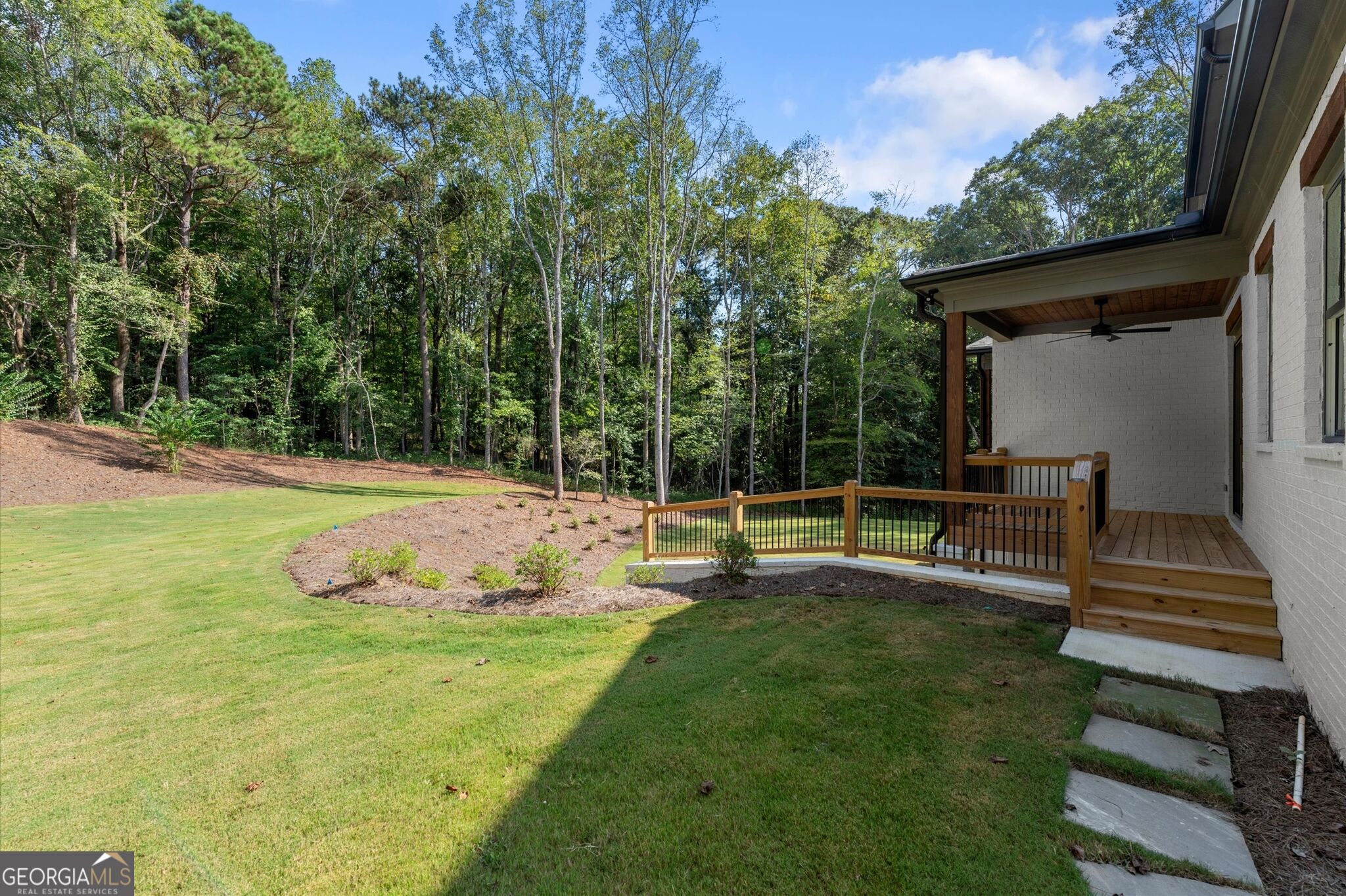 Backyard lawn and covered wooden porch beside a wooded tree line.