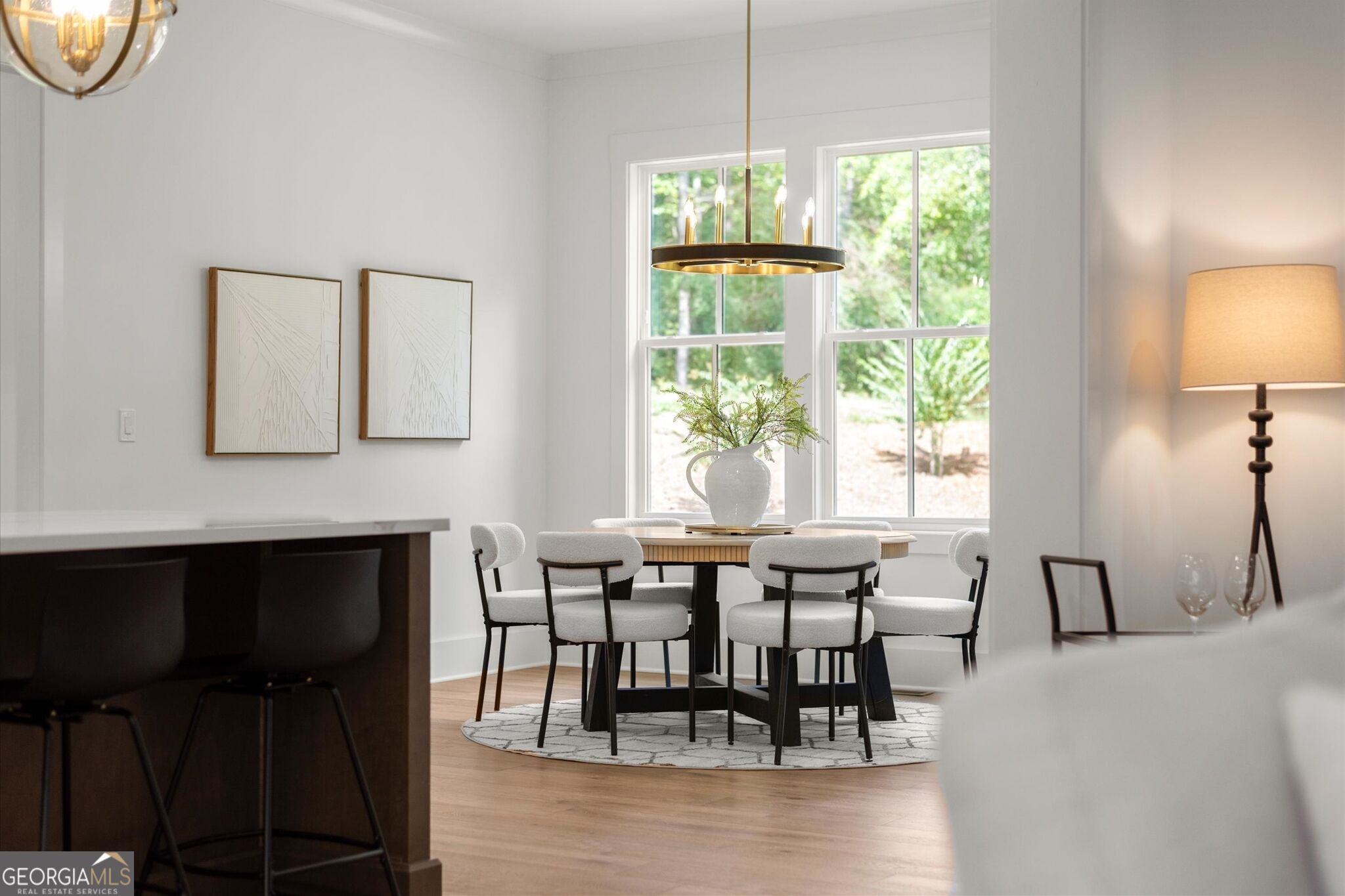 Dining area with a round table, upholstered chairs, large windows, and a dark kitchen island in the foreground.