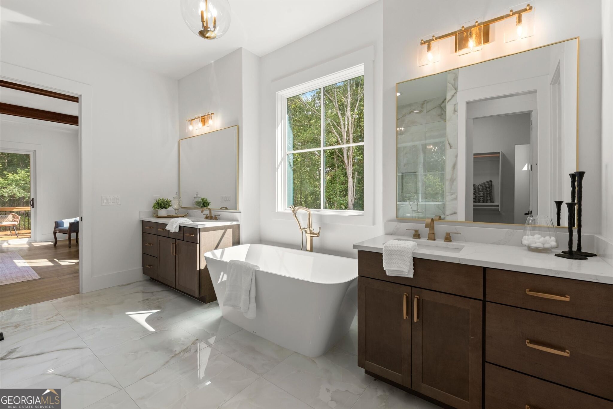 Primary bathroom with a freestanding soaking tub, dark wood vanities, brass fixtures, and a large window.