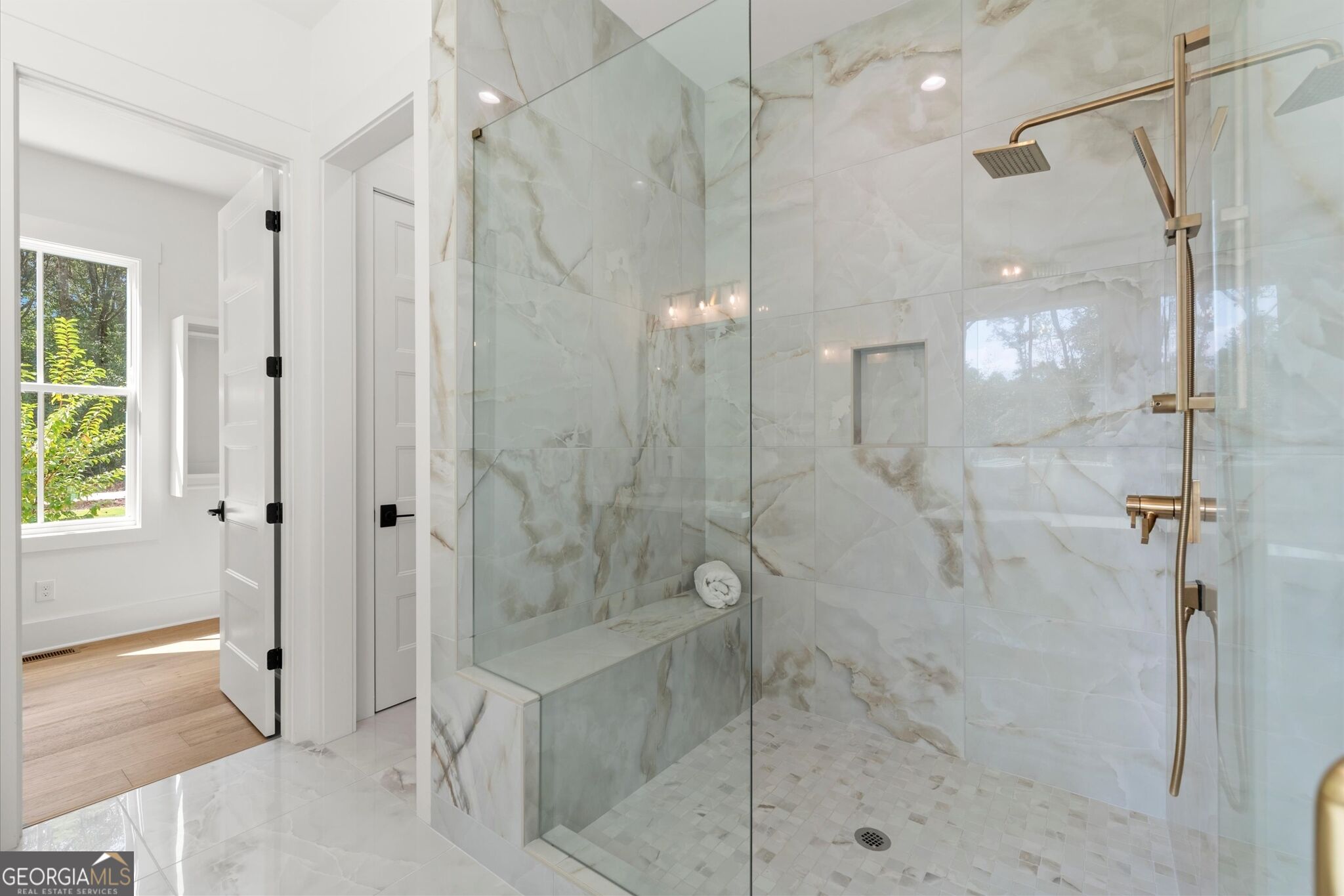 Walk-in shower with marble-look tile, glass enclosure, built-in bench, and bronze fixtures.