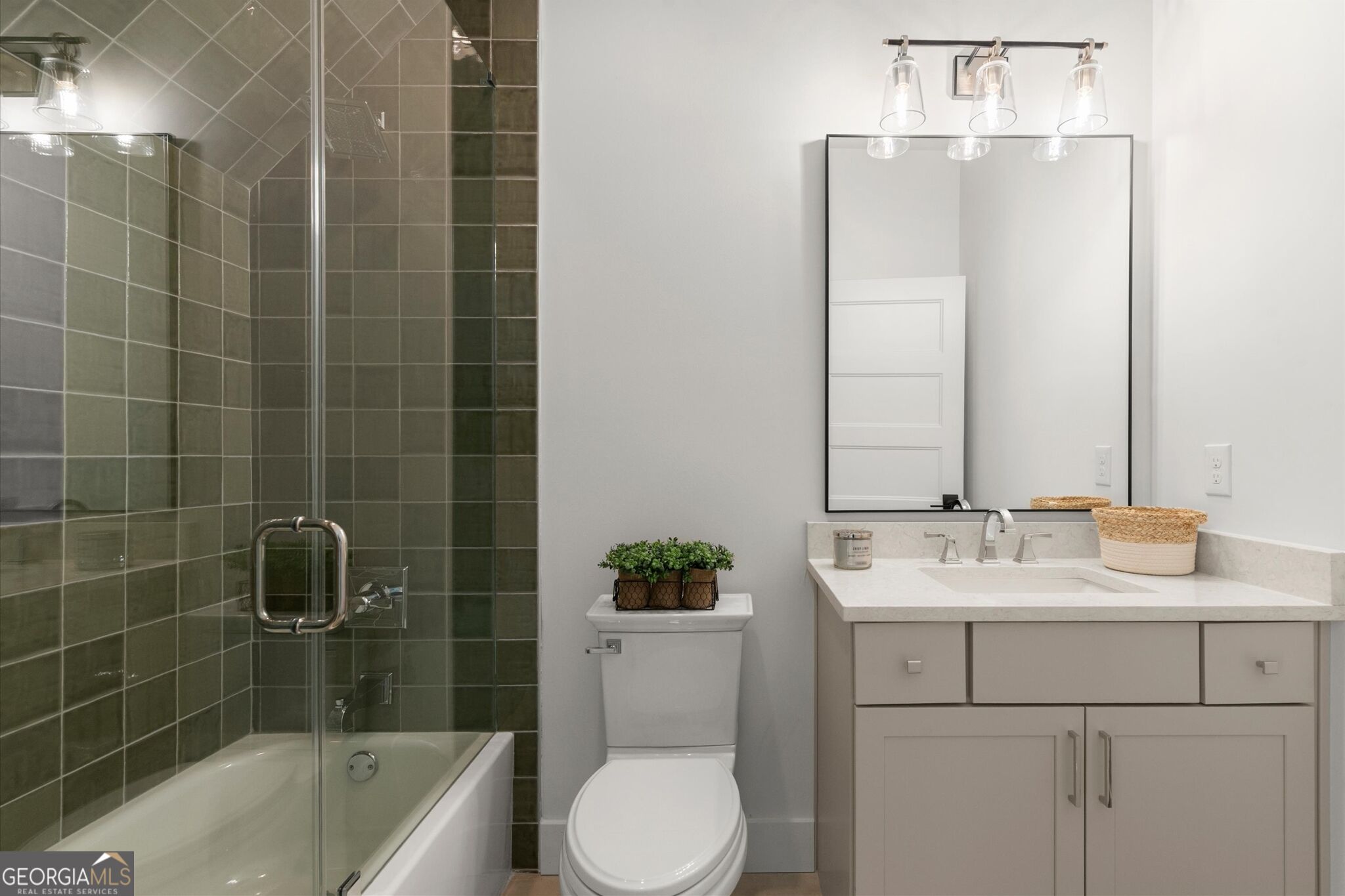 Bathroom with a green-tiled tub and shower, white toilet, and light vanity.
