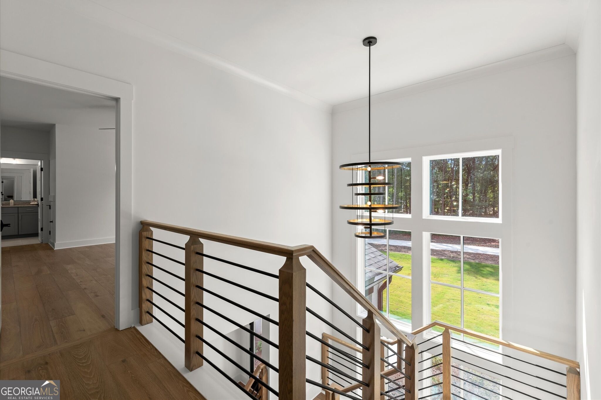 Stairwell landing with wood-and-metal railing, a tiered pendant light, and tall windows overlooking the lawn.